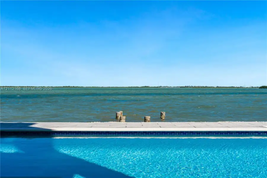 Infinity-edge pool with blue tiled waterline, stone paver decking, and open water frontage Infinity-edge pool with blue tiled waterline, stone paver decking, and open water frontage
