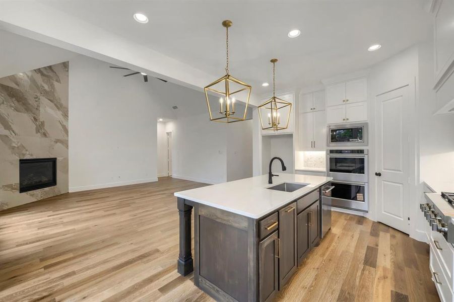Kitchen and living area featuring light wood flooring, a fireplace with a stone-look surround, an island with a white countertop and dark base, and stainless steel kitchen appliances