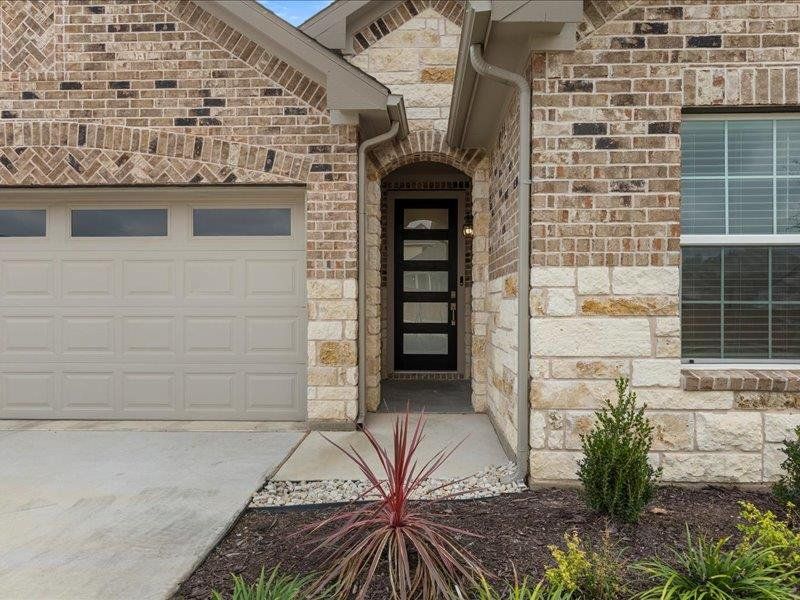 Property entrance with stone siding, driveway, and a garage