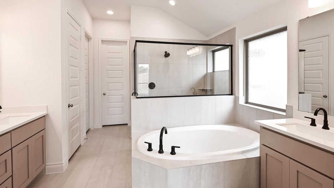 Full bath featuring plenty of natural light, two vanities, tiled shower, lofted ceiling, and recessed lighting