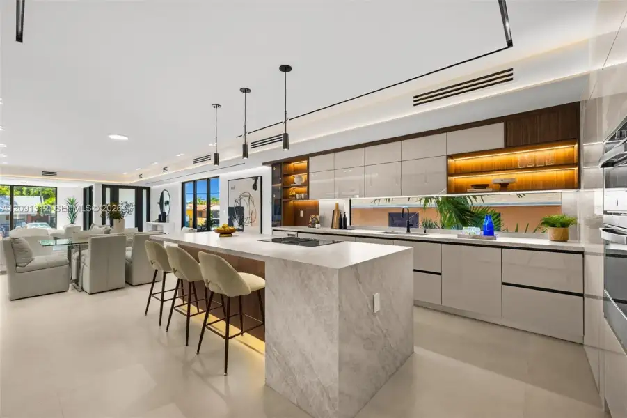 Kitchen featuring a stone-topped waterfall island, flat-panel cabinetry, a horizontal window backsplash, integrated under-cabinet lighting, and porcelain tile flooring Kitchen featuring a stone-topped waterfall island, flat-panel cabinetry, a horizontal window backsplash, integrated under-cabinet lighting, and porcelain tile flooring