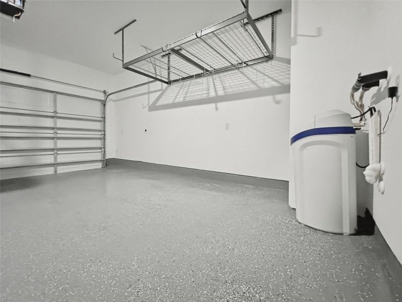 Garage with epoxy-finished flooring, storage, water softener, and EV charging outlet