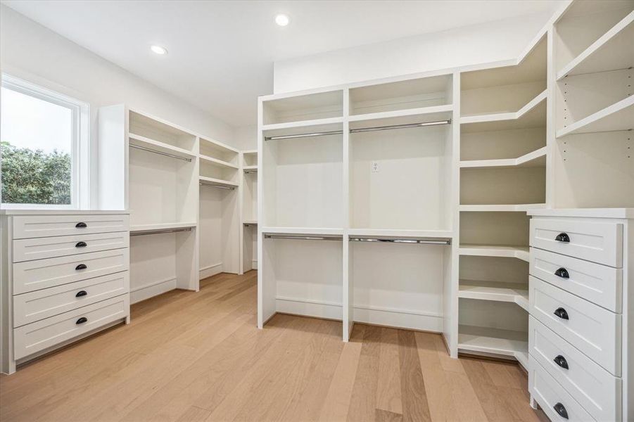 The spacious primary closet is thoughtfully divided into two areas, offering abundant hanging space, a central packing island, dual dressers, and plenty of natural light. Photo as of 7/30/24