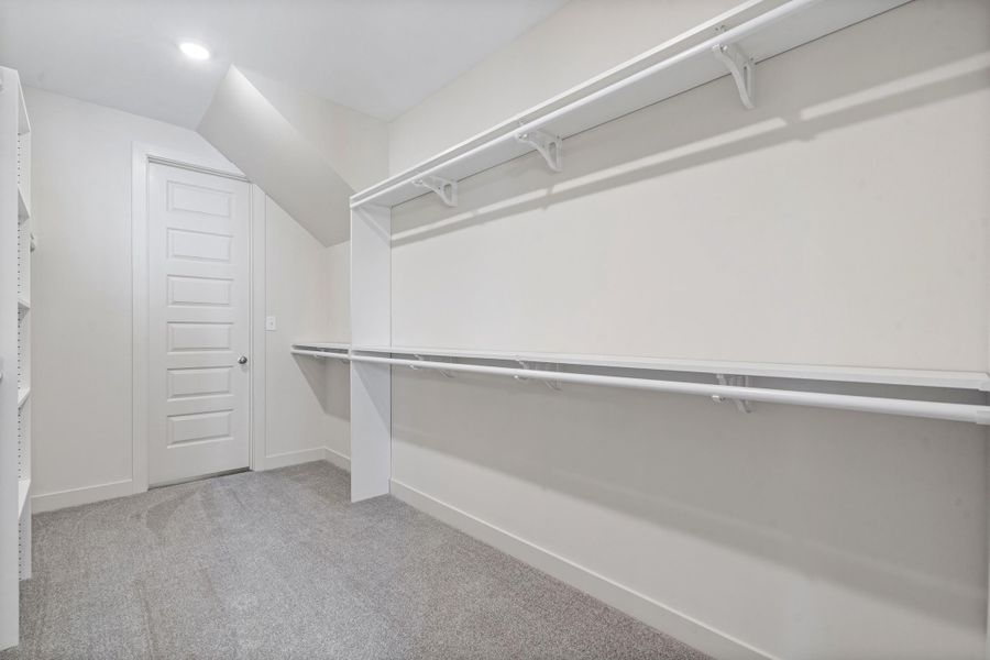 Walk in closet with light colored carpet and lofted ceiling