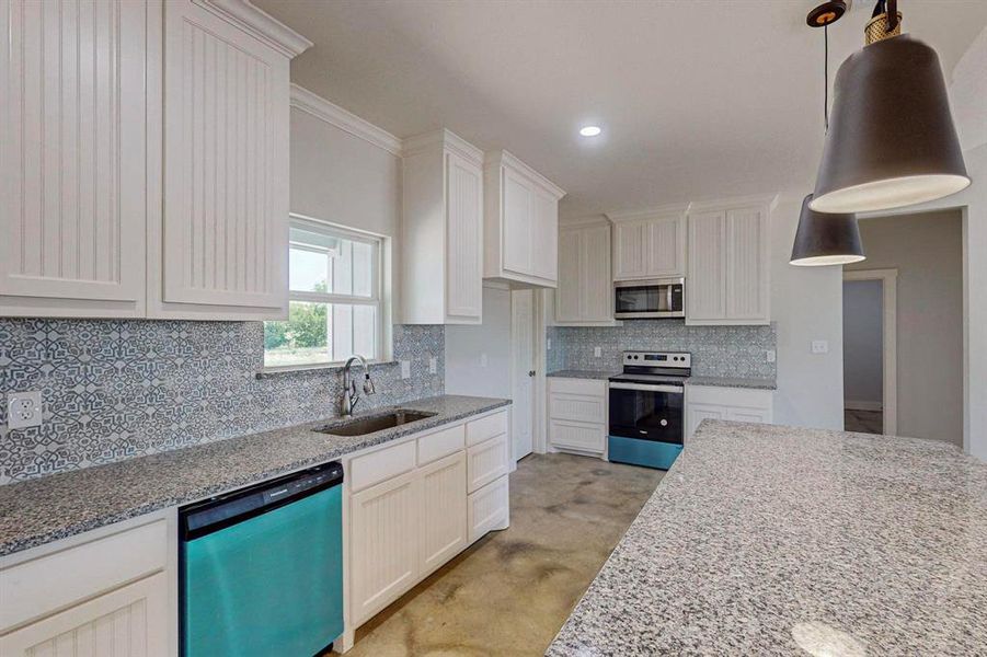 Kitchen featuring appliances with stainless steel finishes, decorative light fixtures, sink, and white cabinets