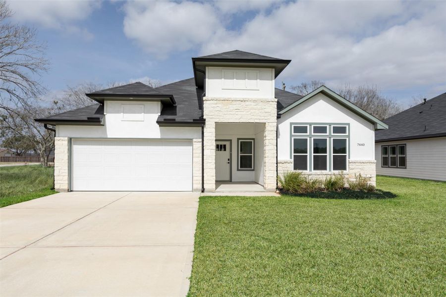 Modern home features a  a clean white facade with stone accents, and a welcoming front porch. Large windows provide ample natural light, and the well-maintained lawn adds curb appeal.