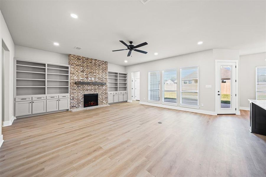 Unfurnished living room with a fireplace, light wood-type flooring, ceiling fan, recessed lighting, and built in features Unfurnished living room with a fireplace, light wood-type flooring, ceiling fan, recessed lighting, and built in features