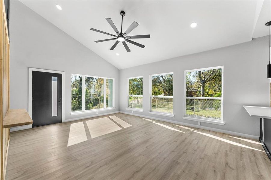 Unfurnished living room with light wood finished floors, ceiling fan, high vaulted ceiling, and recessed lighting