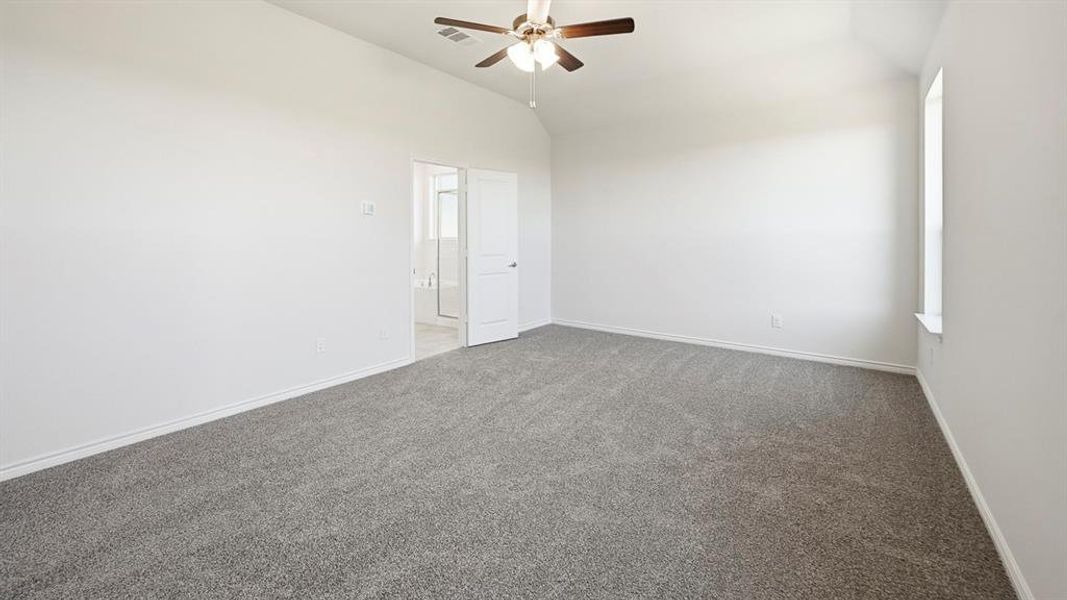 Carpeted spare room featuring vaulted ceiling and a ceiling fan