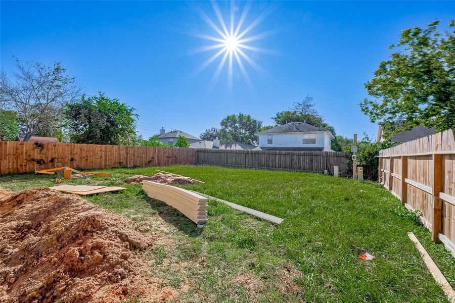 Spacious backyard with wooden fencing, ample green space, and a few construction materials, perfect for customization or landscaping.