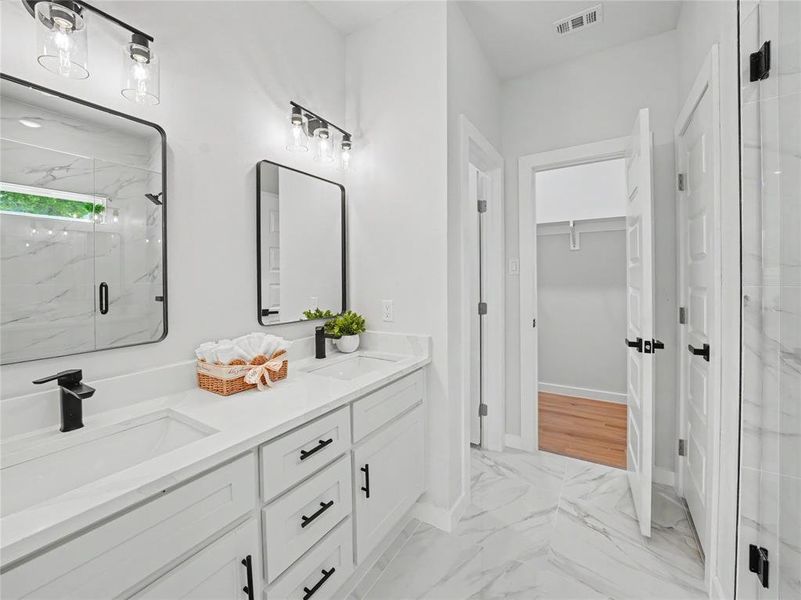 Bathroom featuring a marble finish shower, double vanity, light marble finish floors, and a walk in closet