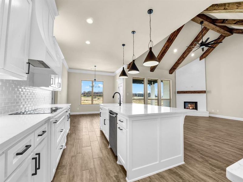 Kitchen featuring a large fireplace, a center island with sink, black electric stovetop, ceiling fan, and white cabinets