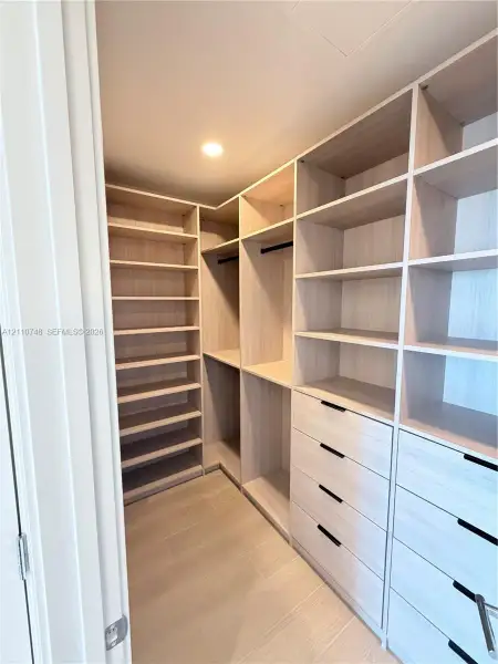 Custom walk-in closet featuring light-toned wood-finish cabinetry, floor-to-ceiling shelving, recessed lighting, and integrated drawers with matte black hardware