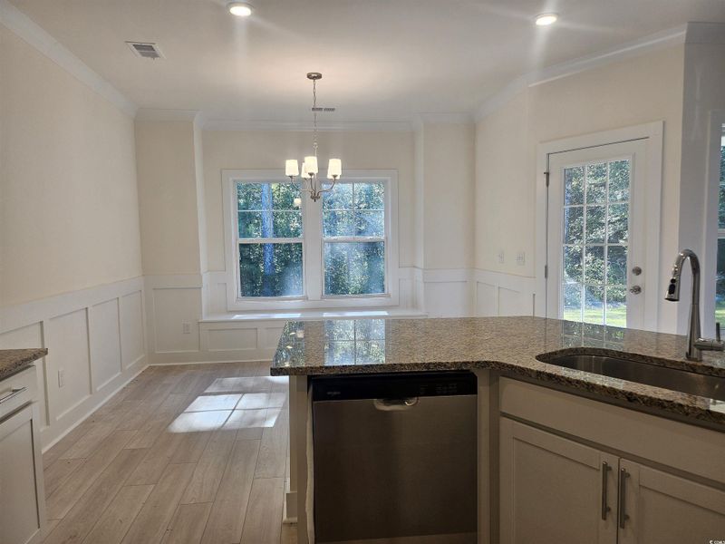 Kitchen featuring dishwasher, a decorative wall, wainscoting, dark stone countertops, and pendant lighting Kitchen featuring dishwasher, a decorative wall, wainscoting, dark stone countertops, and pendant lighting