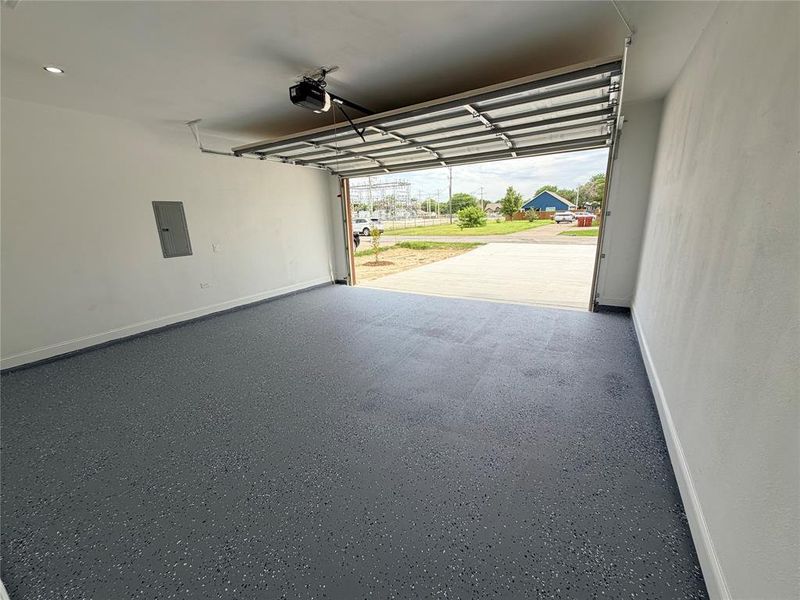 Attached garage featuring a gray epoxy-coated floor, white painted walls, recessed lighting, and an automatic garage door opener Attached garage featuring a gray epoxy-coated floor, white painted walls, recessed lighting, and an automatic garage door opener