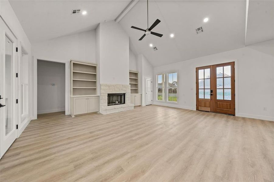 Unfurnished living room featuring french doors, high vaulted ceiling, a stone fireplace, beam ceiling, and light wood-style flooring Unfurnished living room featuring french doors, high vaulted ceiling, a stone fireplace, beam ceiling, and light wood-style flooring
