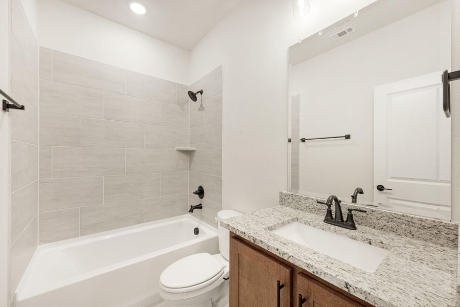Bathroom with tiled tub and shower, granite vanity, wood cabinets, and dark hardware fixtures