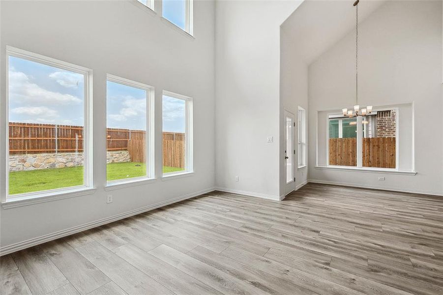 Unfurnished living room with an inviting chandelier, light wood-type flooring, and a towering ceiling