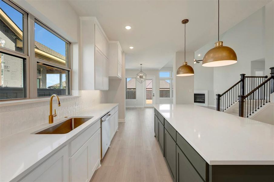 Kitchen featuring two tone cabinets, a glass covered fireplace, light wood-type flooring, hanging lights, and dishwasher