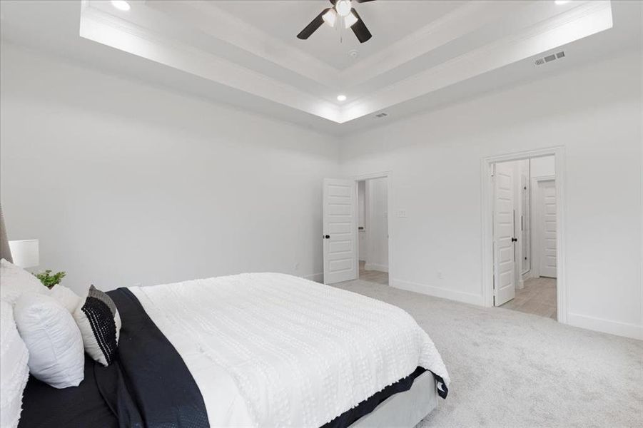 Bedroom featuring light carpet, a tray ceiling, and visible vents