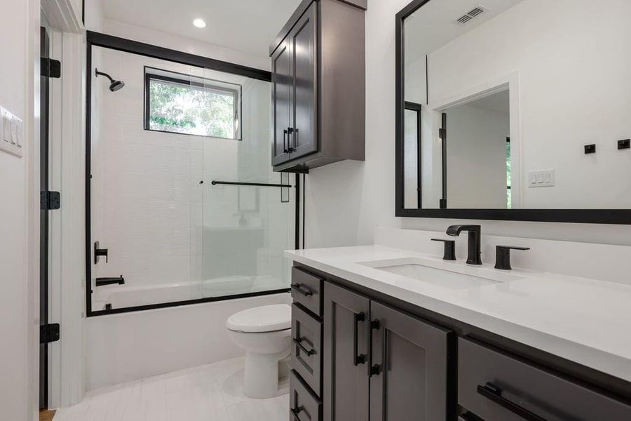 Full bathroom with tile patterned floors, enclosed tub / shower combo, vanity, and toilet