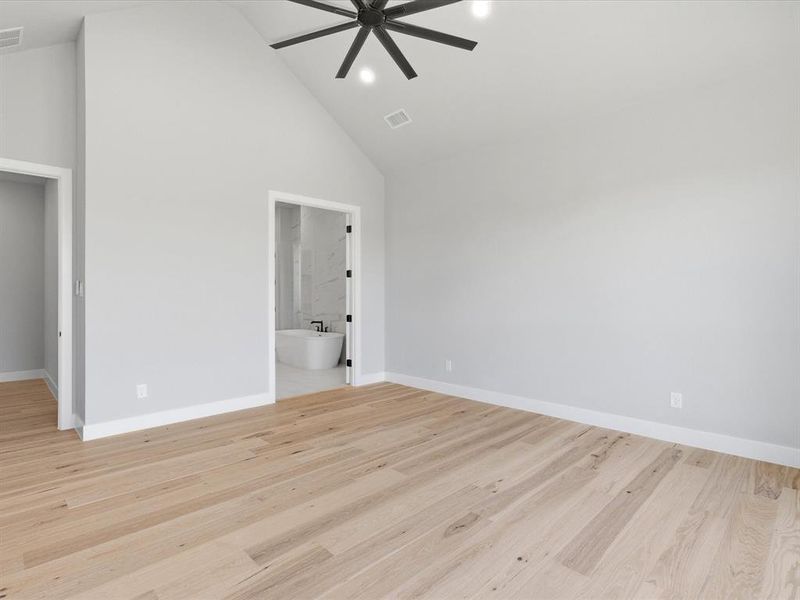 Spacious room featuring vaulted ceilings, light wood-finish flooring, and a modern black ceiling fan with integrated lighting