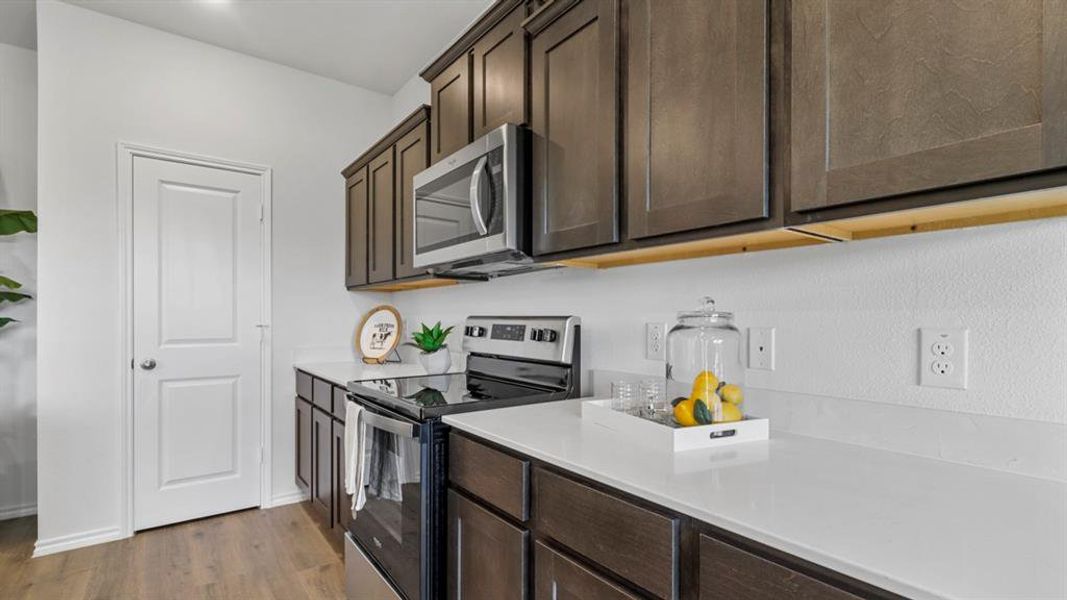 Kitchen with stainless steel appliances, dark wood finish cabinets, light wood-style floors, and light stone countertops