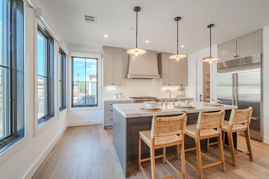 Kitchen with hanging light fixtures, built in fridge, light wood-style flooring, an island with sink, and a breakfast bar area