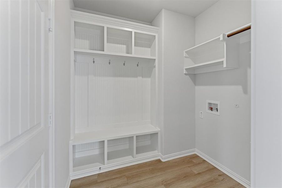 Dedicated utility area featuring wood-finish flooring, white built-in storage with cubbies, upper shelving, and a bench with coat hooks Dedicated utility area featuring wood-finish flooring, white built-in storage with cubbies, upper shelving, and a bench with coat hooks
