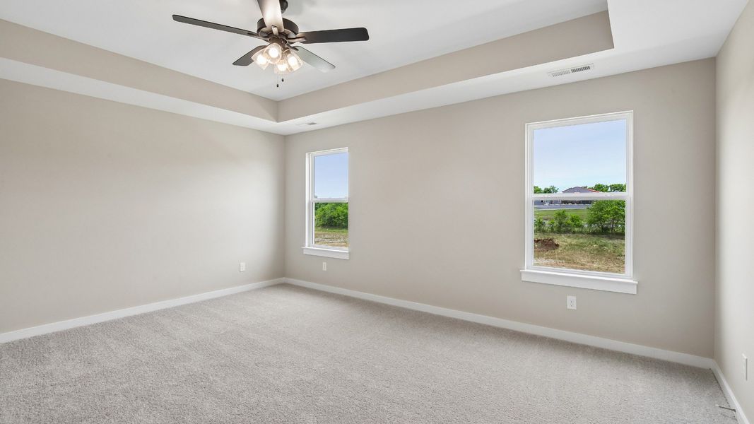 Bedroom with tray ceiling, windows, and en-suite primary bathroom