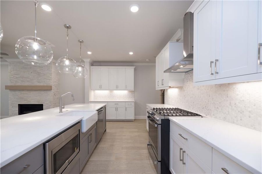 Kitchen with wall chimney range hood, sink, appliances with stainless steel finishes, white cabinetry, and hanging light fixtures