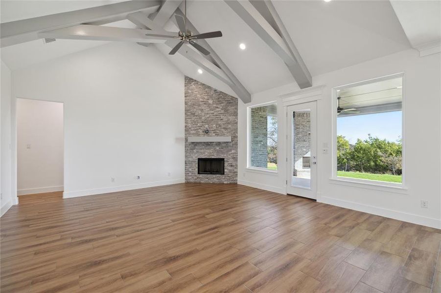 Unfurnished living room with a stone fireplace, plenty of natural light, hardwood / wood-style flooring, and beam ceiling