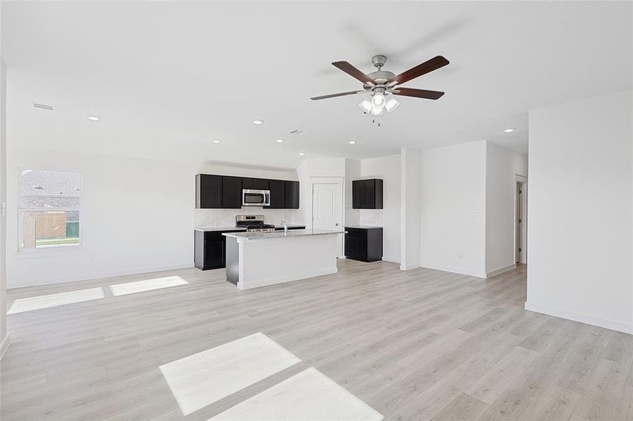 Kitchen featuring ceiling fan, stainless steel appliances, tasteful backsplash, a center island with sink, and light wood-type flooring