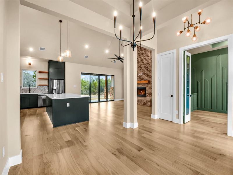 Kitchen with a center island, a brick fireplace, a towering ceiling, appliances with stainless steel finishes, and decorative light fixtures