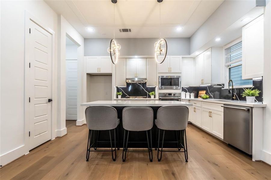 The kitchen is a highlight, featuring a unique pendant lighting arrangement, built-in appliances, a touchless pull-down faucet with smart motion technology, quartz slab backsplash, and a well-designed kitchen island with quartz countertops.