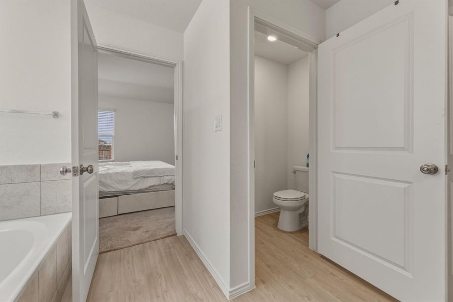 Bathroom area featuring a bathtub with tiled surround and a separate toilet area with light wood flooring