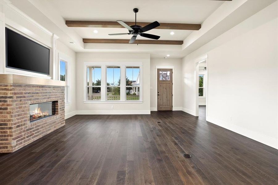 Unfurnished living room featuring ceiling fan, a fireplace, dark hardwood / wood-style flooring, and beamed ceiling