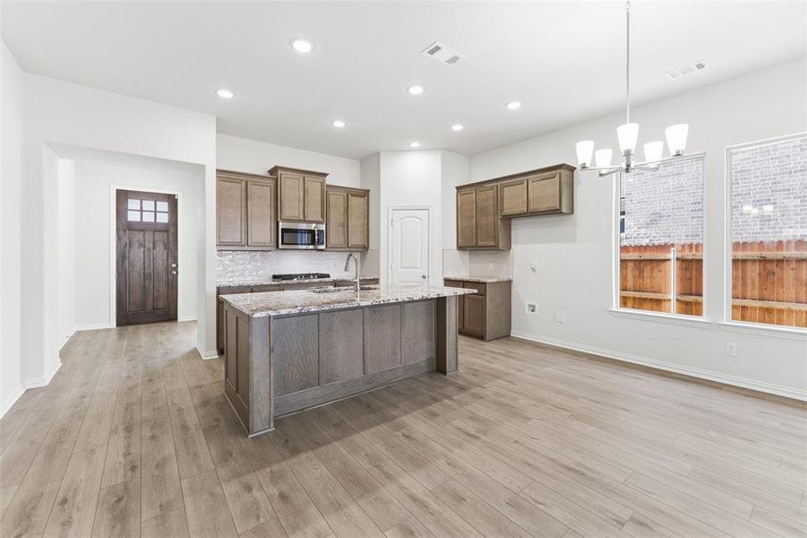 Kitchen with light stone countertops, a chandelier, pendant lighting, a kitchen island with sink, and appliances with stainless steel finishes Kitchen with light stone countertops, a chandelier, pendant lighting, a kitchen island with sink, and appliances with stainless steel finishes