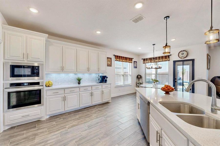 Kitchen with stainless steel appliances, white cabinets, hanging light fixtures, light stone countertops, and recessed lighting