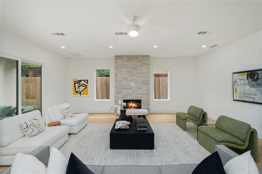 The spacious living area features light wood flooring, a fireplace with a stone surround, and recessed lighting