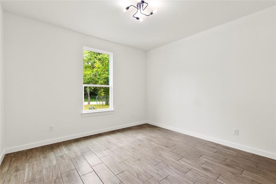 Spacious room featuring wood-finish tile flooring, a large window, a modern ceiling light fixture, white walls, and white baseboards