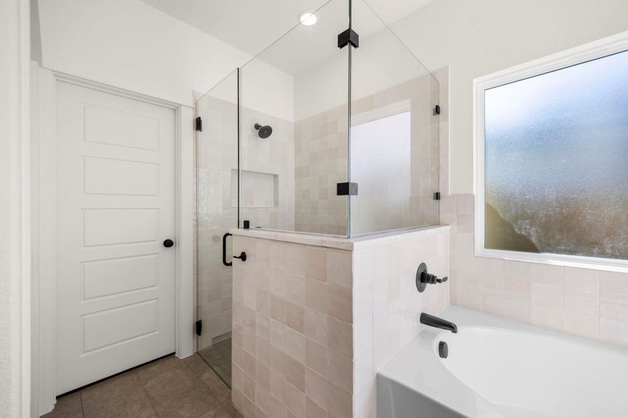 Indulge in a tranquil bathing experience in this sleek, modern primary bathroom, featuring a glass-enclosed shower and a soaking tub.