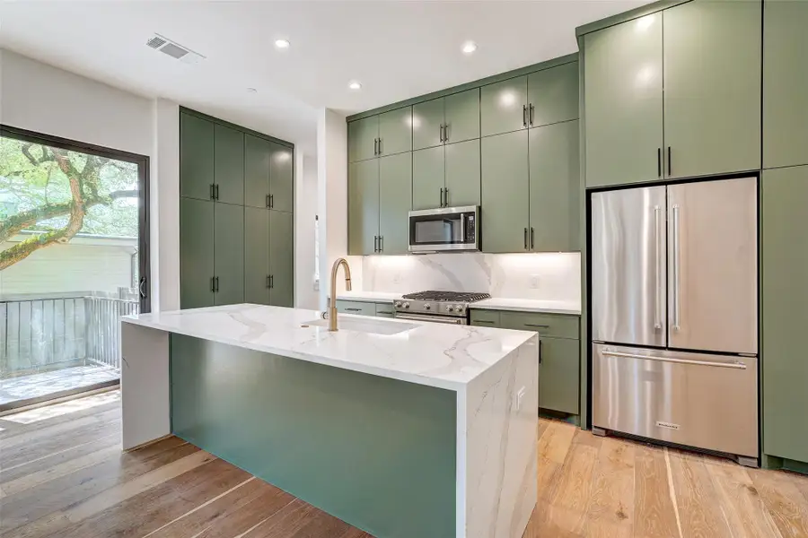 Kitchen with appliances with stainless steel finishes, green cabinets, a sink, light wood-style flooring, and recessed lighting