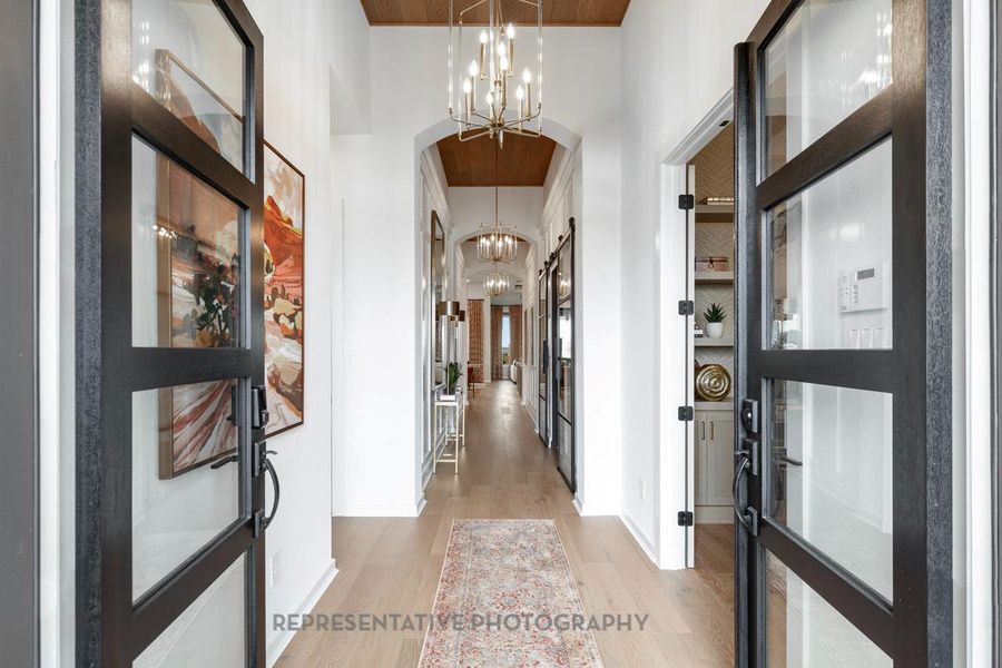 Entrance foyer with a chandelier, light wood-type flooring, a towering ceiling, and arched walkways Entrance foyer with a chandelier, light wood-type flooring, a towering ceiling, and arched walkways