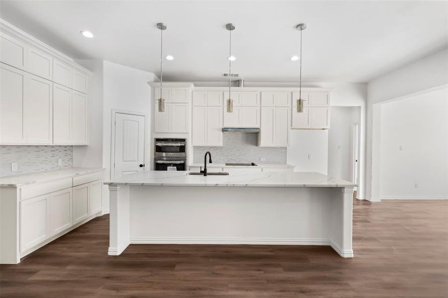 Kitchen featuring dark hardwood / wood-style flooring, decorative light fixtures, a kitchen island with sink, and sink