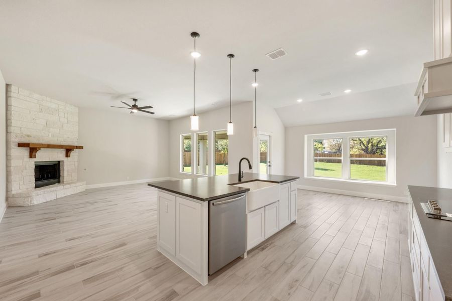 Open-concept kitchen with white island, dark countertops, and stone fireplace in adjoining living area