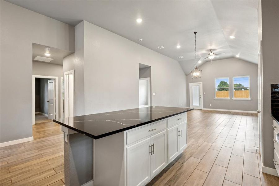 Kitchen featuring white cabinets, a center island, vaulted ceiling, light hardwood / wood-style floors, and dark stone counters