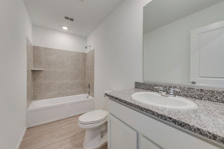 Full bathroom featuring tiled shower / bath combo, hardwood / wood-style flooring, toilet, and vanity