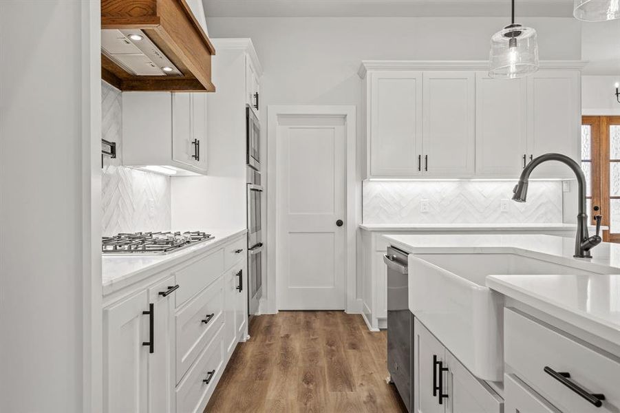 Kitchen featuring backsplash, light countertops, exhaust hood, and white cabinetry Kitchen featuring backsplash, light countertops, exhaust hood, and white cabinetry