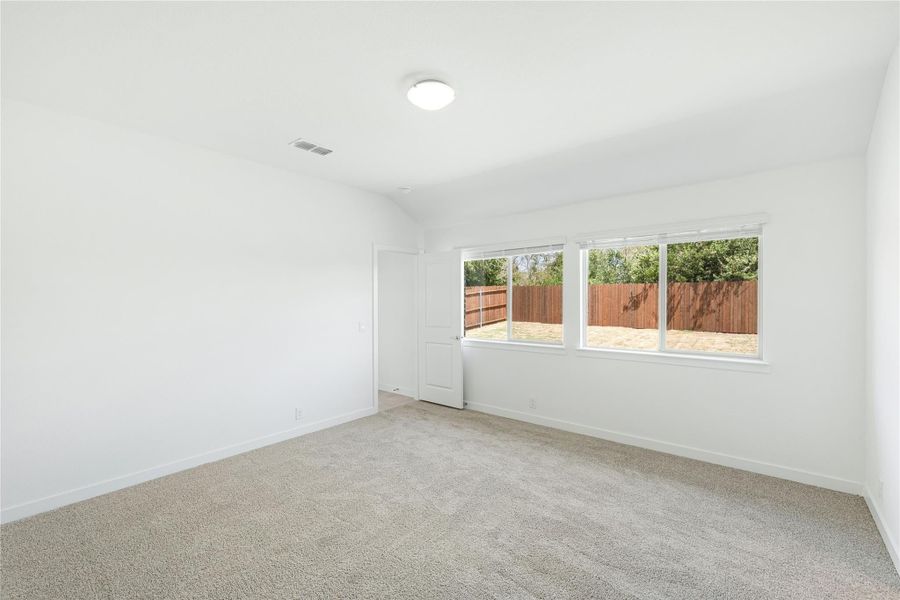 Empty bedroom with beige carpet, white walls, and a window overlooking a fenced backyard